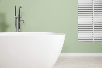 Modern ceramic tub near light green wall in bathroom. Interior design