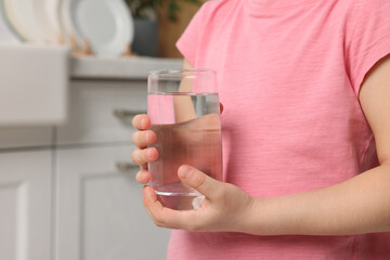 Little girl holding glass of fresh water at home, closeup