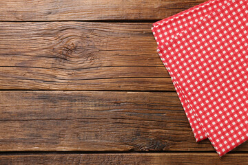 Red checkered tablecloth on wooden table, top view. Space for text