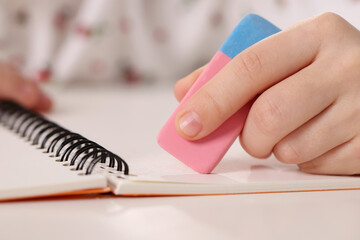 Girl using eraser at white desk, closeup