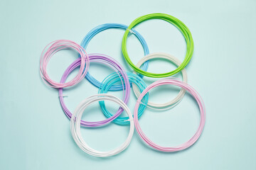 Colorful plastic filaments for 3D pen on light blue background, flat lay