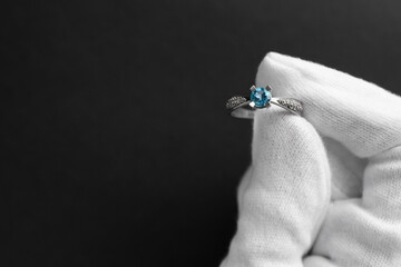 Jeweler holding topaz ring on dark grey background, closeup. Space for text