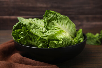Bowl of fresh green romaine lettuces on wooden table, closeup