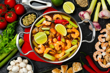 Saucepan with delicious Tom Yum soup and ingredients on black marble table, flat lay