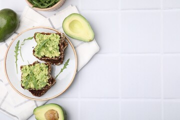 Delicious sandwiches with guacamole, arugula and avocados on white tiled table, flat lay. Space for text