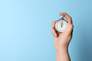 Woman holding vintage timer on light blue background, closeup. Space for text - obrazy, fototapety, plakaty