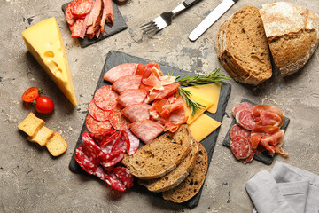 Slate plates with assortment of tasty deli meats, bread and cheese on grey background