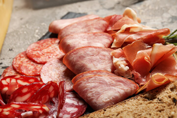 Slate plate with assortment of tasty deli meat on table, closeup