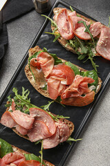 Board of tasty bruschettas with ham on grunge background, closeup