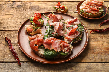 Plates of tasty bruschettas with ham on wooden background