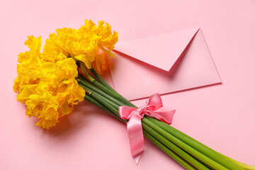 Beautiful narcissus flowers with pink ribbon and envelope on color background