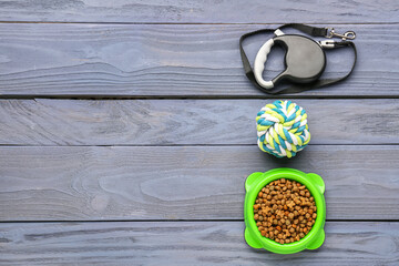 Bowl of dry pet food, leash and toy on color wooden background
