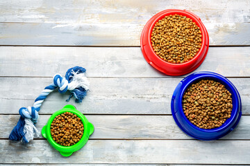 Bowls of dry pet food with toy on light wooden background