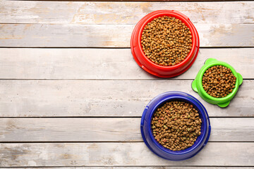 Bowls of dry pet food on light wooden background