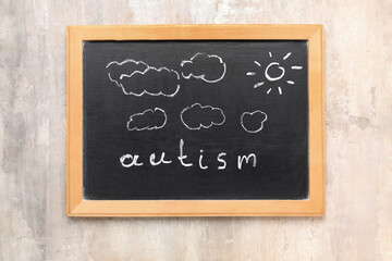 Chalkboard with word AUTISM, drawn clouds and sun on grunge background
