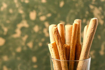 Glass with tasty Italian Grissini on green grunge background, closeup