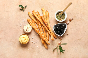 Tasty Italian Grissini with bowls of olives, herbs and sauce on beige background