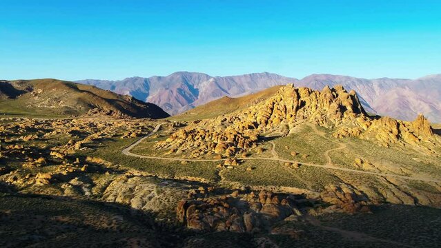 Aerial Shot Of Tranquil Rock Formations Against Clear Sky, Drone Flying Backwards Over Semi Arid Desert On Sunny Day - Alabama Hills, California