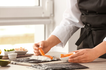 Obraz na płótnie Canvas Woman preparing sushi rolls at table, closeup