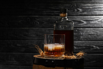 Bottle and glass of cold rum on barrel against dark wooden background