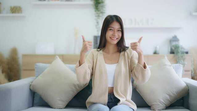 Happy teen asian girl blogger smiling face waving hand talking to webcam recording vlog, social media influencer streaming, making video call at home. She thumb up good or better