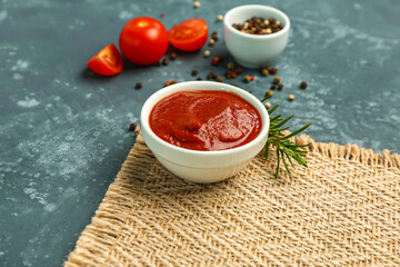 Bowl with tasty tomato paste, rosemary and peppercorn on grey grunge background