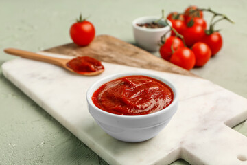 Board with bowl of tasty tomato paste and fresh vegetables on green grunge background