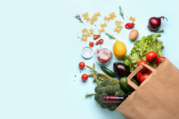 Paper bag with vegetables, wine bottle and lemon on blue background