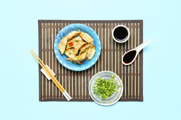 Plate with tasty Chinese jiaozi, onion and sauce on blue background