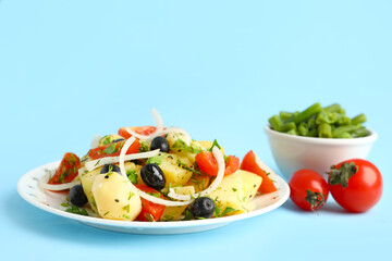 Plate of tasty Potato Salad with vegetables on blue background