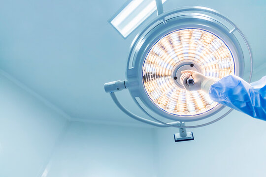 Doctor or surgeon in blue gown holding surgical lamp to adjust light inside operating theatre with space in background.People did surgery in hospital.Nurse with medical glove in operating room.