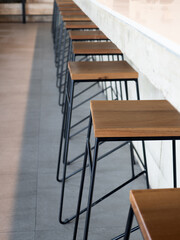 Row of wooden bar stool chairs beside concrete counter bar, loft style cafe interior, vertical style. Empty wood seats with black steel bar decoration on concrete floor.