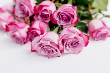 A bouquet of beautiful pink roses with a white gold engagement ring with diamonds on a white background. Fresh flowers on a white canvas. Wedding bouquet and wedding rings. Surprise marriage proposal.