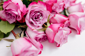 A bouquet of beautiful pink roses with a white gold engagement ring with diamonds on a white...
