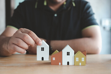 Man hand choosing mini wood house model from model on wood table, Planning to buy property. Choose the best loan concepts. Finance ideas, real estate investments and home mortgage loans.