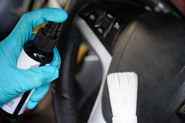 Car detailing. employee sprays a spray bottle of disinfectant on a soft white brush to clean the steering wheel.