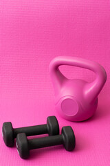 Vertical view of black dumbbells and pink kettlebell in Pink background