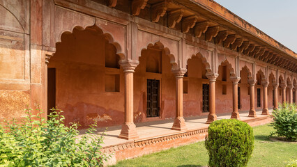 Fototapeta premium Gallery in the Taj Mahal complex. Terrace, columns, arches made of red sandstone. Wooden doors at the entrance to the premises. Green bushes on the lawn. India. Agra