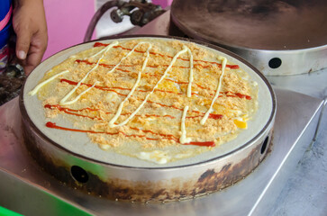 Cooking crepe dessert with topping, egg, dried shredded pork, ketchup, mayonnaise in street food market Thailand.