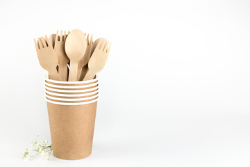 Wooden forks and spoons in a paper cup on a white background. Eco-friendly disposable kitchen utensils. Zero waste concept. Top view. Copy space.
