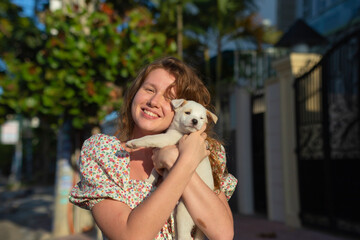 young girl with a small dog in her arms, white puppy in the arms woman walks in the summer on the street