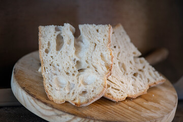 Rustic homemade sourdough bread slices set on a round wooden board, healthy and tasty loaf with a beautiful golden crust and a light and airy crumb structure derived from the low fermentation process