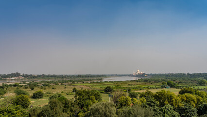 Fototapeta na wymiar View from the Red Fort, the Musamman Burj Tower on the Taj Mahal. Green Valley. The white marble mausoleum is reflected in the lake. Blue sky. India. Agra.