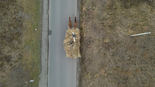 Aerial view of pair of horses pulling old wooden cart full of dry hay with peasant men on it