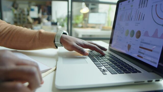 Cropped shot of hands of African American financial analyst working with data on laptop at office desk