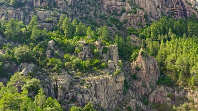 The aerial view of Aiguilles de Bavella in Corsica displays a striking landscape of rugged granite peaks, verdant forests, and winding rivers, creating a dramatic and picturesque natural scenery.