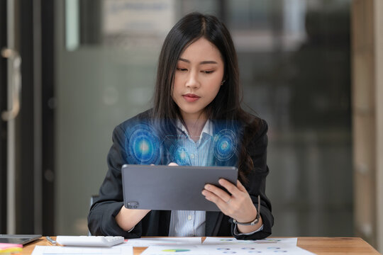 Portrait of an Asian businesswoman in a casual suit using a technology tablet for working via futuristic screen hologram in a modern office, Business owner and entrepreneur concept.