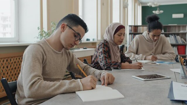 Ethnically diverse immigrant students sitting at table in library making notes during language class