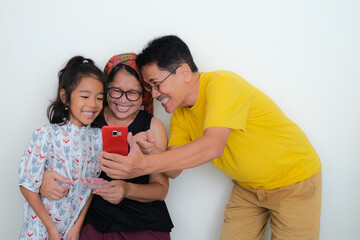 An Asian family with one daughter looking at the father's cellphone smiling excitedly.