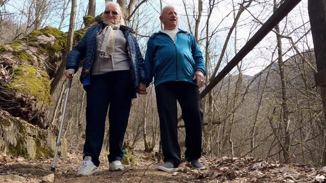 Romantic couple of elderly seniors hiking with crutches on the forest